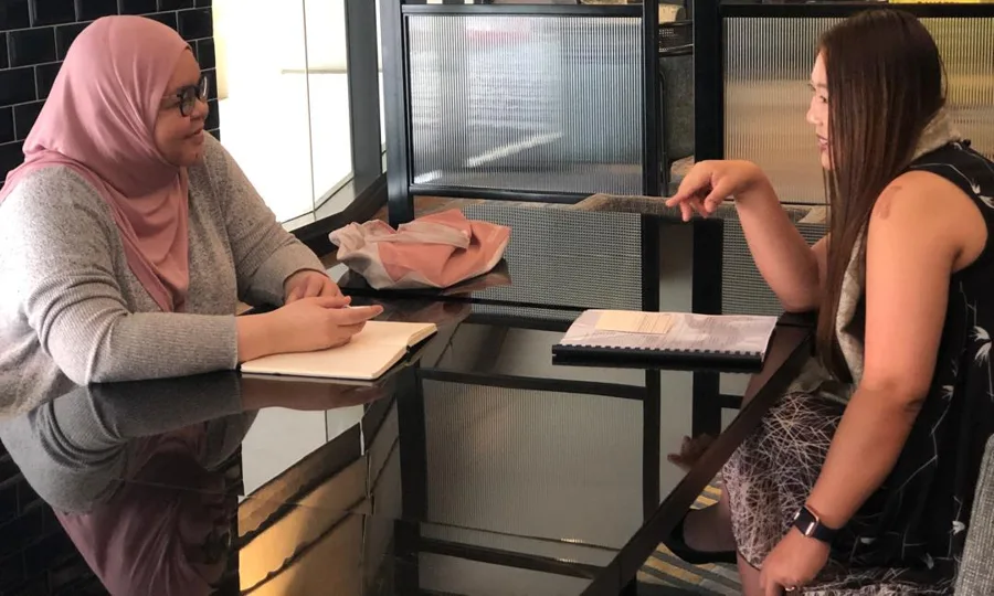 Two leaders in a peer advisory conversation at a table, notebooks open